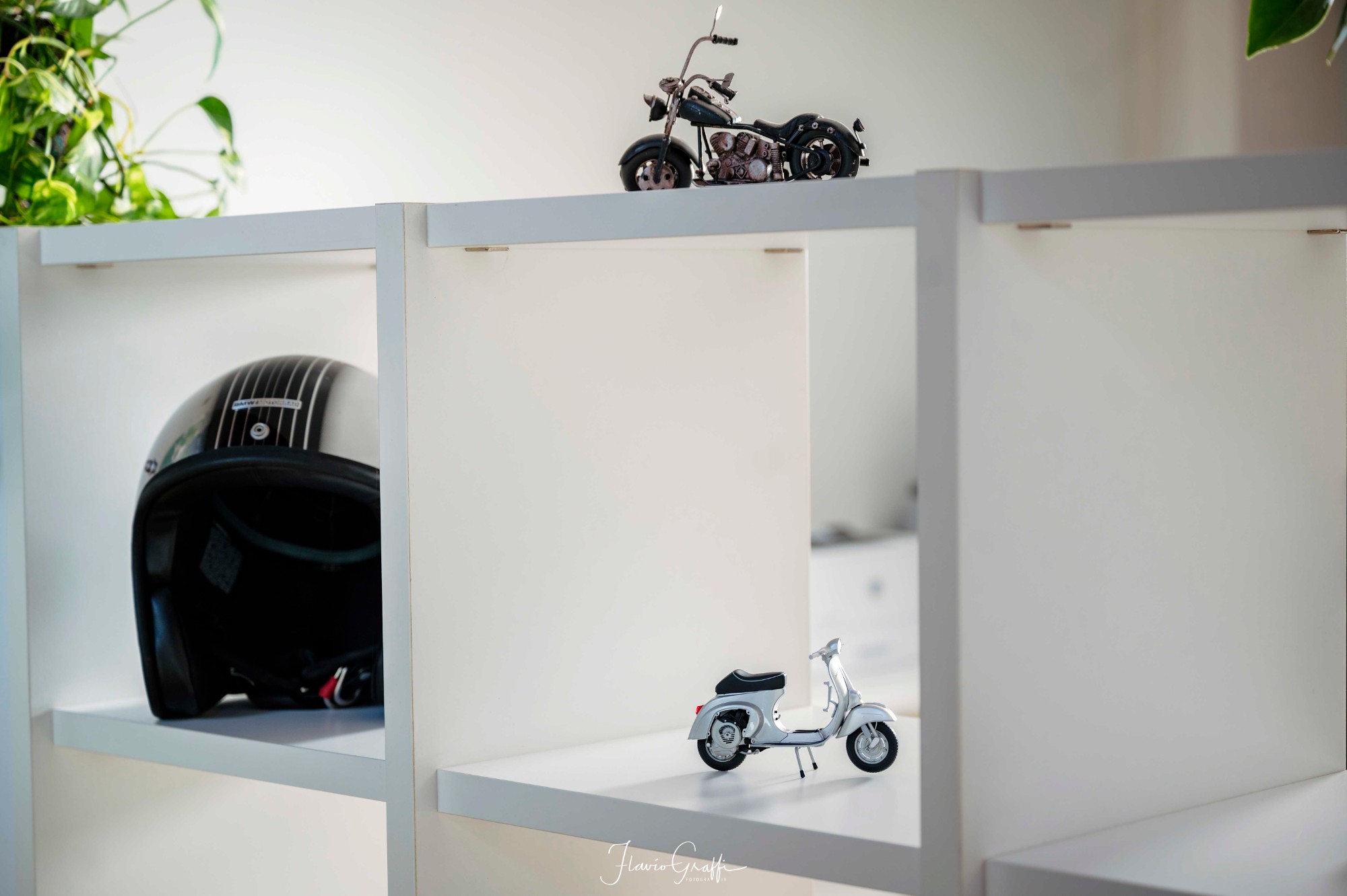 A helmet and a model Vespa on a white shelf